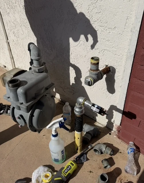 Pump system with brass fittings, valves, and PVC connections mounted on white exterior wall