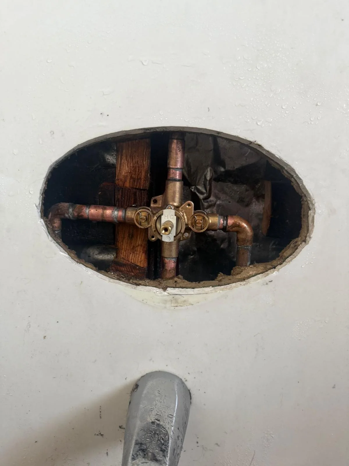 Brass shut-off valve with copper supply lines and wooden backing installed in drywall opening
