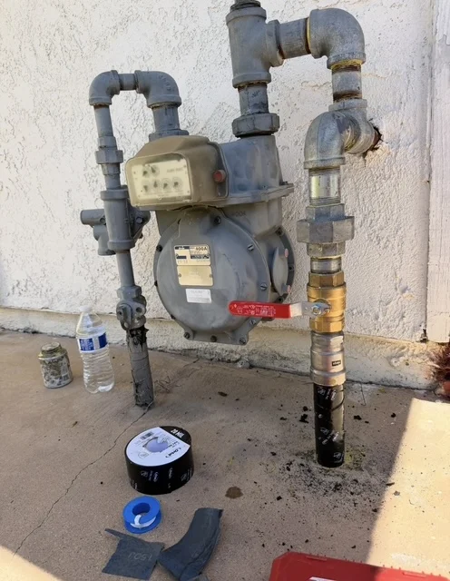 Gas meter assembly with regulator, black iron pipes, and shutoff valves mounted on exterior wall