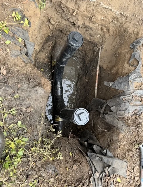 Black corrugated sewer pipe with cleanout caps installed in excavated trench with soil backfill