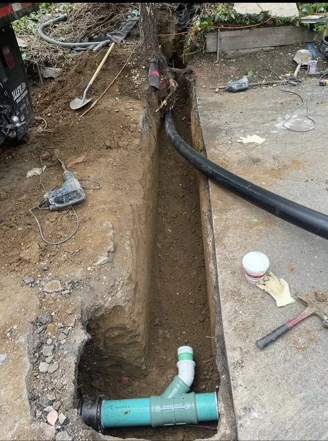 Trench excavation with green PVC sewer pipe and white fittings installed underground